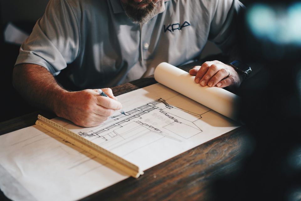 Plan technique au crayon et règle — geste précis de l'artisan qui dessine la stratégie digitale avant de construire
